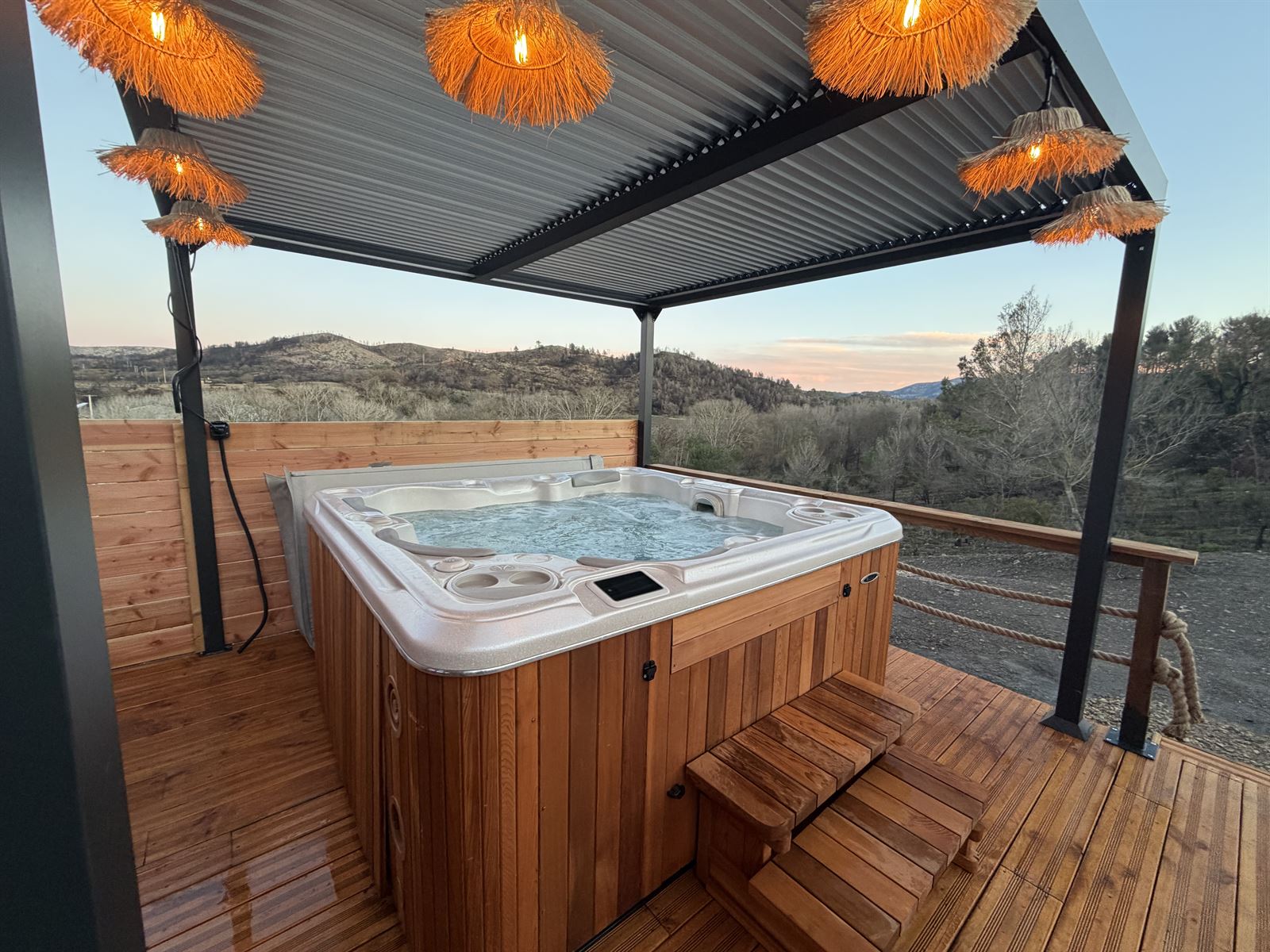 Jacuzzi de L'Amoré sous la pergola, éclairé par des suspensions en raphia au coucher du soleil