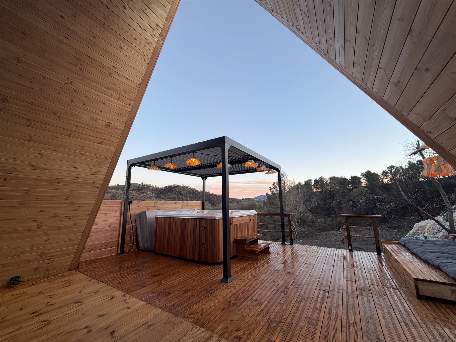 Terrasse de L'Amoré vue depuis l'intérieur, avec la pergola et le jacuzzi au coucher du soleil